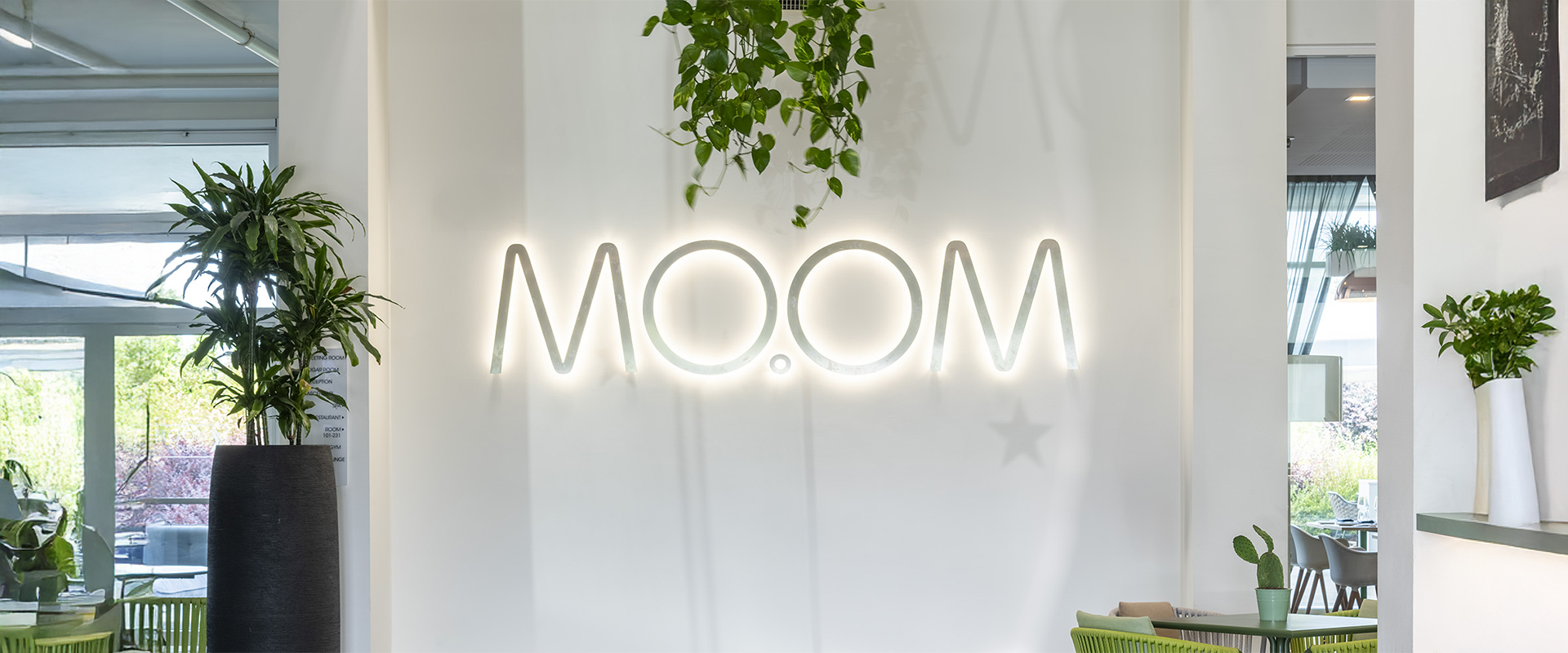 Logo luminoso MOOM all’ingresso, circondato da piante verdi