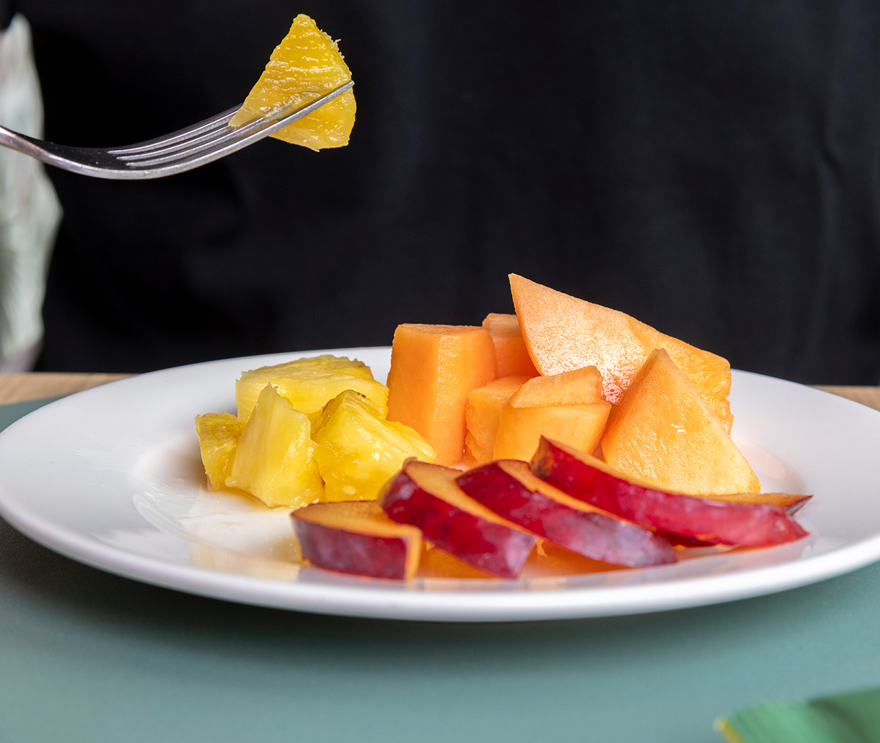 Primo piano di un piatto bianco con frutta fresca assortita: melone, ananas e pesche a fette
