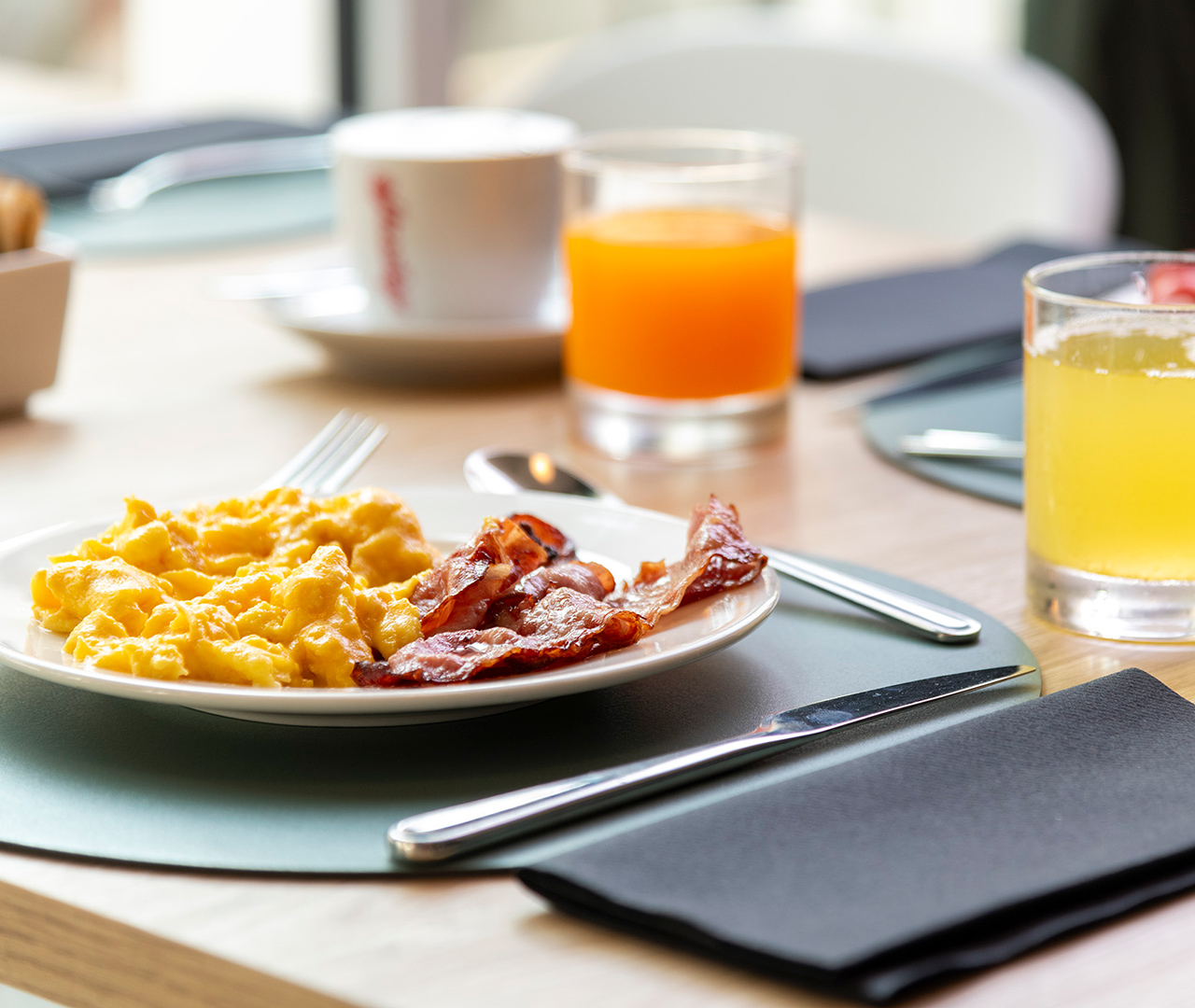 Colazione all'americana servita al tavolo, con uova strapazzate, bacon e succo d'arancia