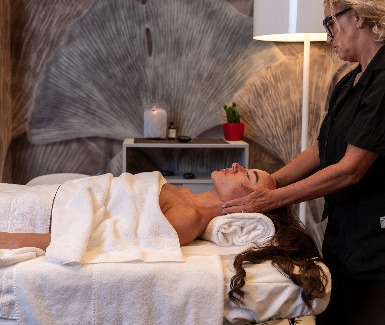 Massaggio al viso eseguito da un’operatrice su una donna distesa in cabina spa.