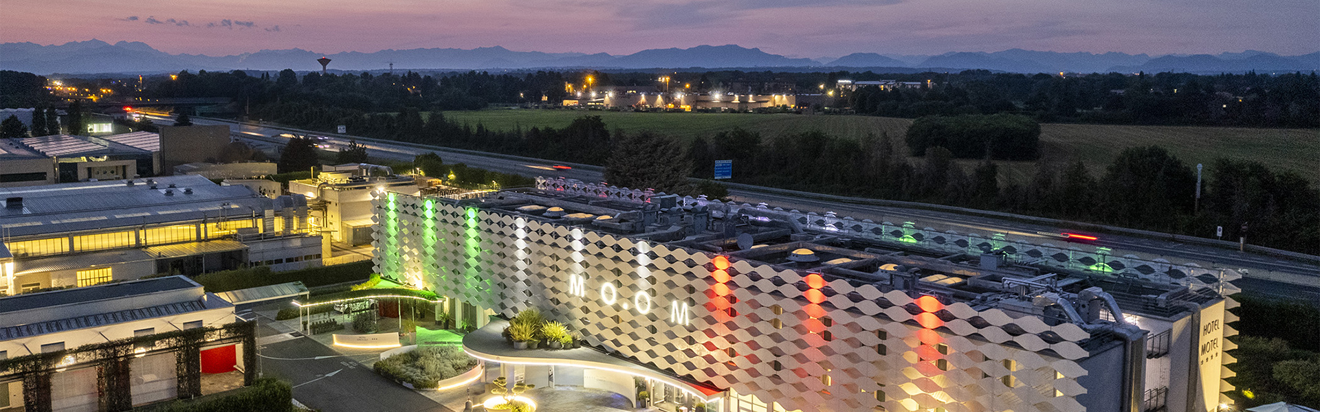 Veduta panoramica serale del Moom Hotel, con la sua facciata di design illuminata con il tricolore