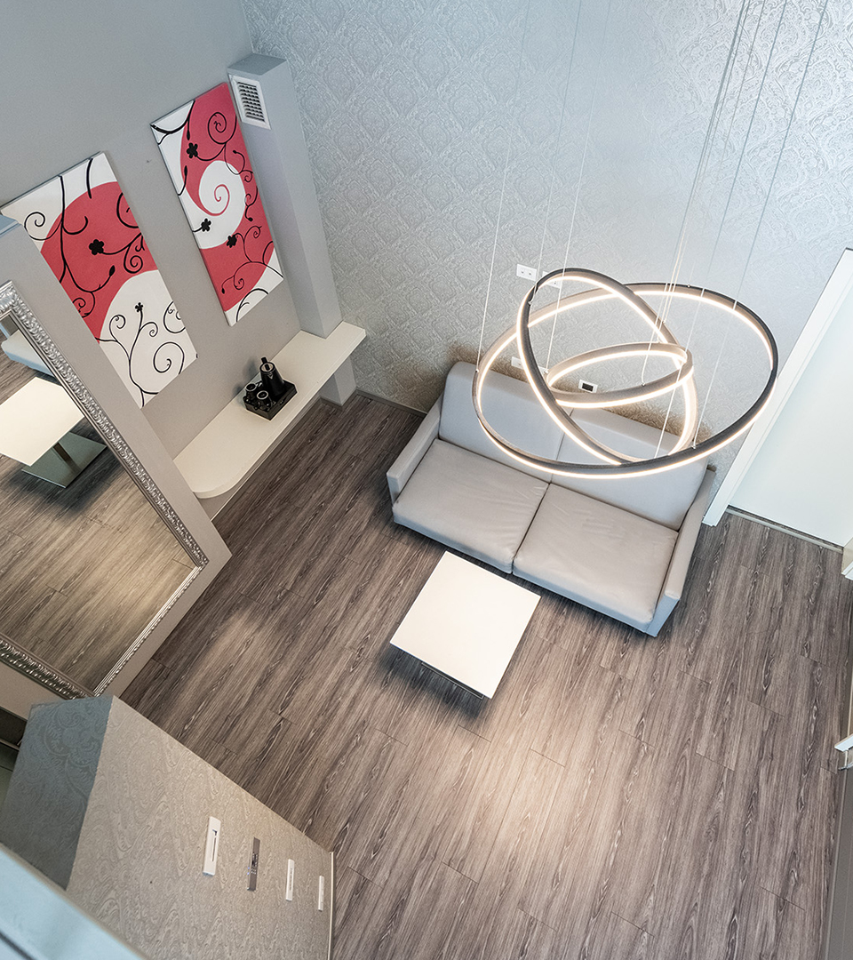 Elegante soggiorno di una suite con pavimento in legno, divano grigio, lampade circolari e quadri astratti rossi