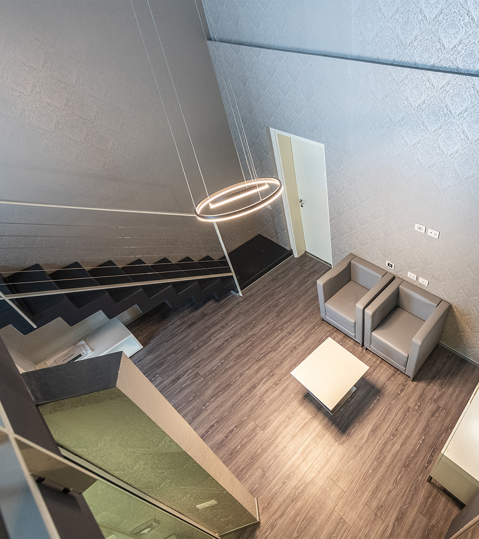 Suite su due livelli con zona living al piano inferiore, scala interna, poltrone con tavolino centrale e lampada a sospensione circolare di design